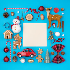 Christmas holiday decorative border frame made with candy cane, ornaments, snowman, deer and gingerbread man on blue background. Minimal winter or New Year concept with copy space. Flat lay, top view.