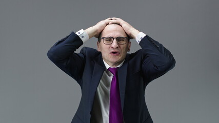 Shocked middle aged office worker in formal clothes, tie and glasses feeling stressed with hands on head, shame and sad face, tragic and frustrated. Fear and upset for mistake, people emotions concept