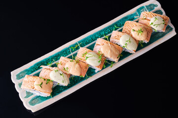 .rolls with baked salmon on a black background with a corrugated plate.
