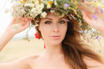 beautiful woman with a wreath on her head sitting in a field in flowers. The concept of beauty, free life and naturalness