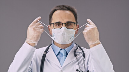 Handsome male lab technician in medical uniform takes off protective mask against covid-19 virus, germs, bacteria and happy smiles on isolated white background. Victory over coronavirus, protection