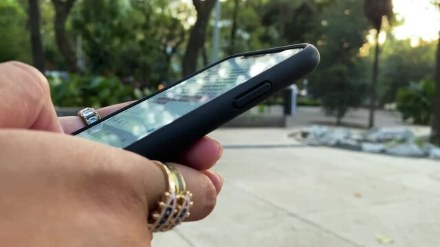 A young woman is texting meanwhile she is at the park.