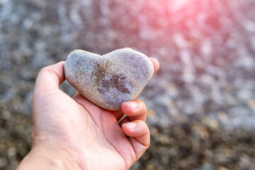 hand with a stone in the form of a heart against a background of wet pebbles on the beach....
