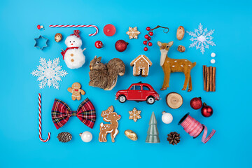 Christmas holiday decorative layout made with candy cane, ornaments, snowman, deer and gingerbread man on blue background. Minimal winter or New Year concept with copy space. Flat lay, top view.