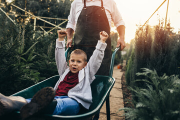 grandfather giving grandson ride in wheelbarrow in tree nursery