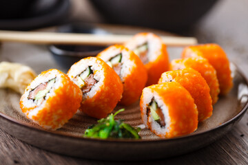 Sushi maki rolls with salmon, avocado, cucumber, flying fish roe on a plate with chopsticks, soy sauce, wasabi and ginger. Japanese traditional food served for lunch in modern gourmet restaurant