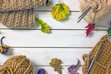 Knitting autumn composition flat lay. Skeins of brown wool, knitting needles, a knitted scarf, fallen leaves, acorns, chestnuts on a woody background. Handicraft concept, making warm handmade things