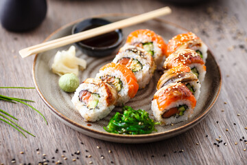 Sushi maki rolls with salmon, eel, avocado, cucumber on a plate with chopsticks, soy sauce, wasabi and ginger. Japanese traditional fish food closeup served for lunch in modern gourmet restaurant