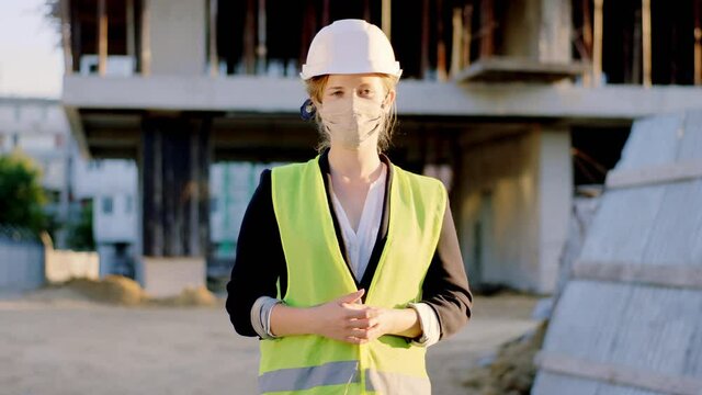 Attractive blonde hair lady architect with a safety helmet with protective mask in the pandemic Coronavirus posing in front of the camera at construction site