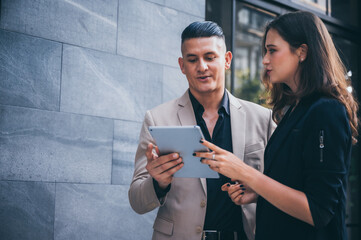 Two business people walking and discussing at the street outdoor by using the tablet for online...