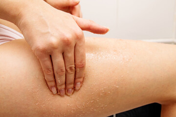 Naklejka premium In the frame, the girl's hand scrubs the skin of her thigh with salt for massage