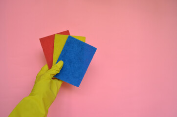 Female hand  in yellow rubber glove with colored washcloths on pink background. Cleaning or housekeeping concept background. Copy space. Flat lay, Top view.