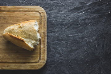 Top view of half-plucked Turkish bread on wooden chopping board on dark grey grunge background with copy space.
