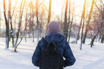 Close up young hipster man with backpack on his shoulder walking in winter snowy park. back view. atmospheric moment