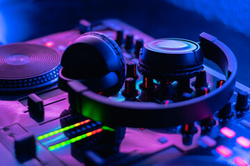 Fototapeta na wymiar Mesa controladora de sonido con auriculares de DJ encendida con colores morados y azules