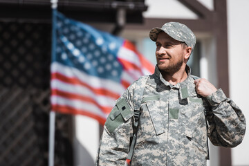 Smiling military veteran in camouflage looking away with blurred american flag on background