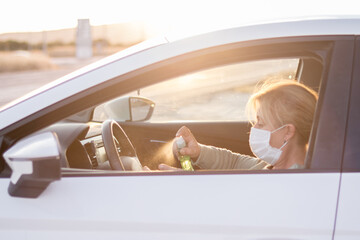 Mujer con mascarilla en su vehículo desinfectándose las manos