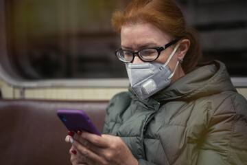 Mature woman in respirator mask use a smartphone and keep social distancing in subway. Concept of new life reality during  COVID 19 pandemic             