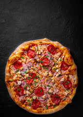 Pizza with Mozzarella cheese, salami, chicken meat, bacon, ham, Tomato sauce, pepper, spices. Italian pizza on Dark grey black slate background