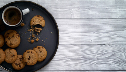 Flat lay of homemade chocolate chip cookies on plate with a fresh hot cup of coffee on wooden table simple morning snack copy space