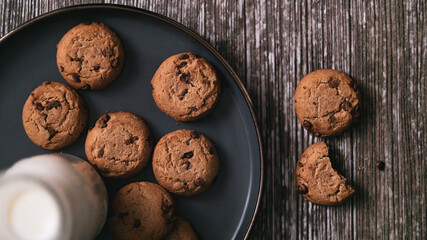Flat lay of a bitten chocolate chip cookie and a bottle of milk with crumbs on wooden table simple morning breakfast snack c
