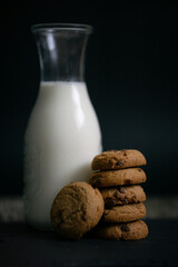 Close up view of  chocolate chip cookies and a bottle of milk with crumbs on wooden table simple morning breakfast snack