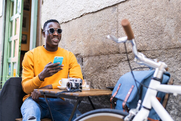 Fototapeta na wymiar Black Tourist Man Using Cellphone Sitting in in a Cafe.
