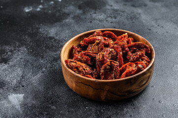 Sun dried tomatoes  in wooden bowl. Black, dark background. Top view. Copy space