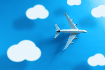 Top view of a commercial plane with clouds and long shadow on a blue background.