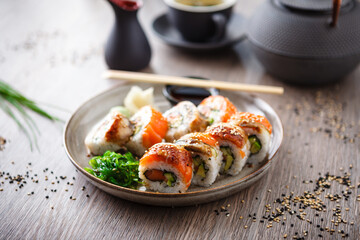 Sushi maki rolls with salmon, eel, avocado, cucumber on a plate with chopsticks, soy sauce, wasabi and ginger. Japanese traditional fish food closeup served for lunch in modern gourmet restaurant