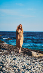 Portrait of a girl with red hair developing in the wind with an open neckline against the background of the sea