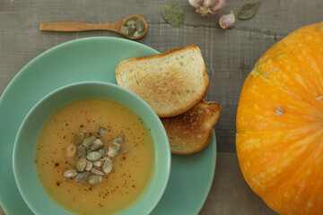 Healthy pumpkin cream soup with spices, garlic, croutons and bread on a gray tabletop background. Autumn still life