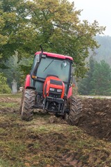 Obraz premium Red tractor on a muddy field. Agricultural work. Autumn foggy morning on the farm. Agriculture machinery.