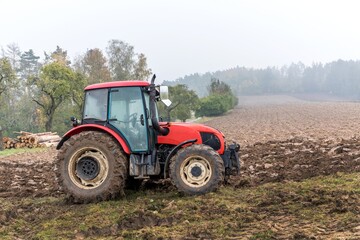 Red tractor on a muddy field. Agricultural work. Autumn foggy morning on the farm. Agriculture machinery.