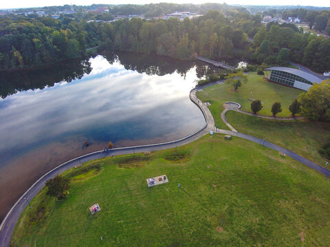 A Gorgeous Aerial Shot Of The Still Lake Waters, Bike Trails, Playgrounds Green Grass, Lush Green And Autumn Colored Trees, Parked Cars At Rhodes Jordan Park At Lawrenceville Lake In Lawrenceville