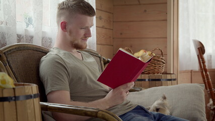 Young handsome guy male student in casual wear resting on home, sitting at sofa enjoying reading...
