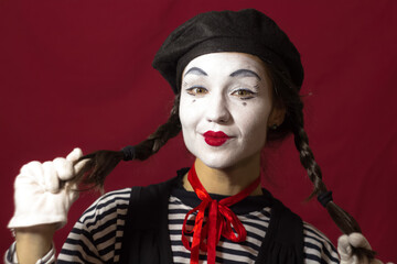 Beautiful mime girl smiles and holds her pigtails with her hands.