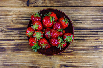 Ceramic plate with pile of ripe strawberries on wooden table. Top view