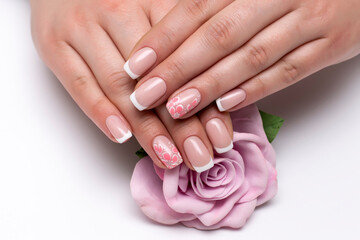 Obraz na płótnie Canvas Classic French manicure on short square nails with flowers on the ring fingers. Wedding nail designs. Pink rose in hands.