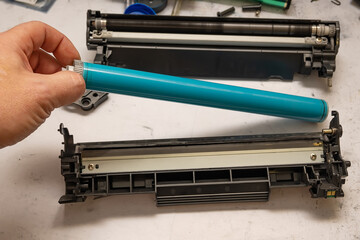 the hand of the service center master holds an organic selenium photoreceptor by the gear while refilling the laser printer cartridge