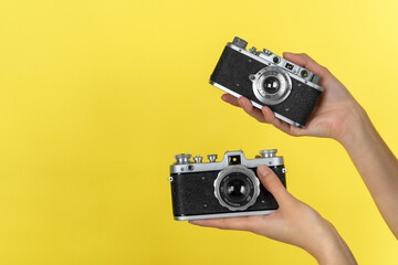 two hands holding two vintage photo cameras on a yellow background with a space for a text.