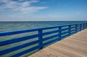 Obraz premium Pier from boards with blue fence against the sea and blue sky with clouds on a sunny day, copy space