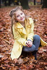 Little beautiful girl in a yellow raincoat walks in the  park.