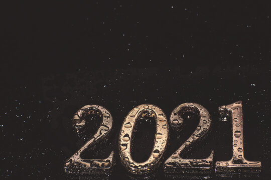 Metallic numbers 2021 in golden color covered with water droplets on a dark background