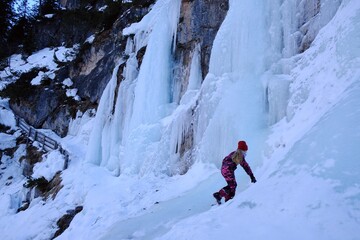 Beautiful winter view - frozen waterfall and silhouette of climbing child by the lake Lago di Braies, Alta Pusteria, Dolomites, Italy