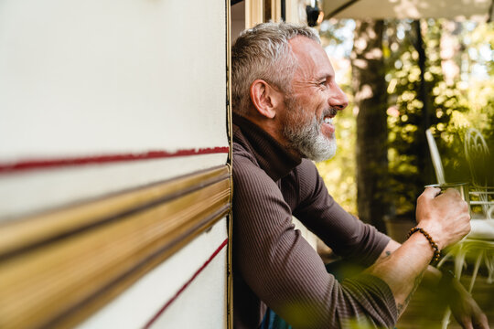 Close up side view portrait of a senior handsome man with cheerful smile and a mug of tea sitting on the porch of his trailer