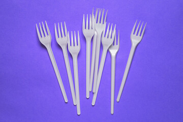 Fototapeta na wymiar White plastic forks on a purple background. Disposable tableware for a picnic, lunch or dinner. A top view of a flat layout