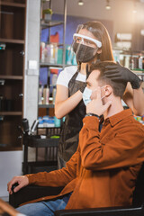 barber in face shield and latex gloves touching hair of client pointing with finger