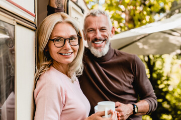 Close up shot of pleased senior caucasian couple smiling at the camera with cups of coffee standing...