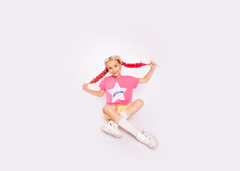 .cute girl in bright colorful clothes and with colored braids sits with a skateboard